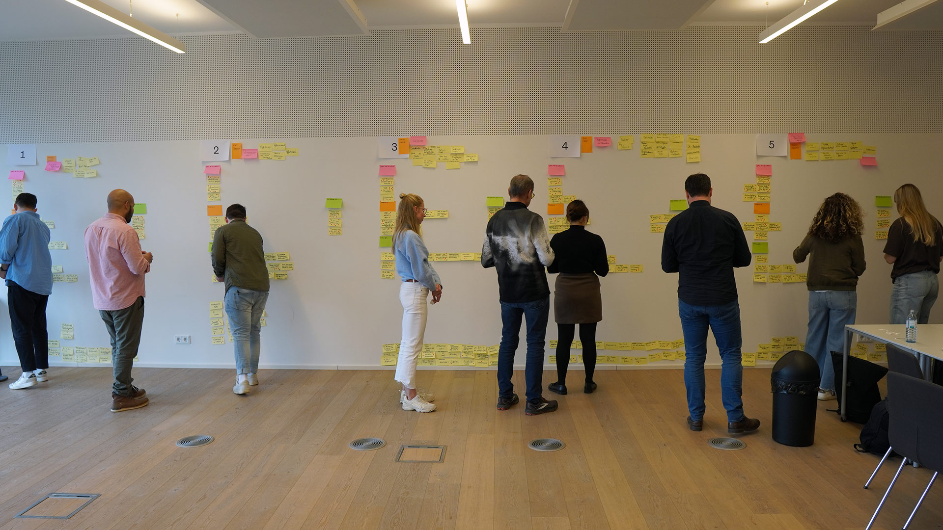 Eine Gruppe von Menschen, die an einer weißen Wand befestigte Haftnotizen anschauen.