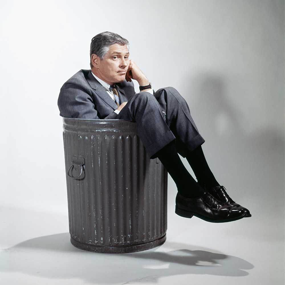 Ein Mann sitzt mit betrübtem Blick in einer Mülltonne.