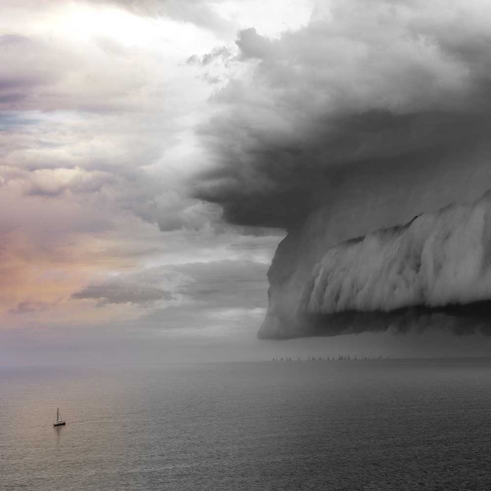 Ein Photo eines kleinen Segelbootes auf dem offenen Meer mit einer Sturmfront am Horizont.